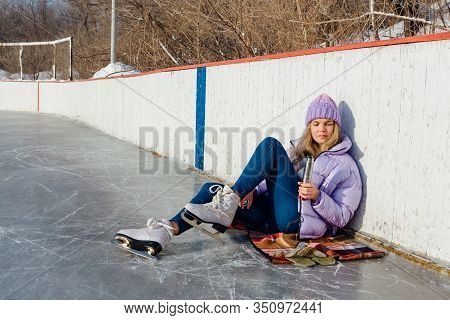 Lovely Young Woman Relaxing After Riding Ice Skates And Drinking Hot Drink From Termo Pot On The Ice