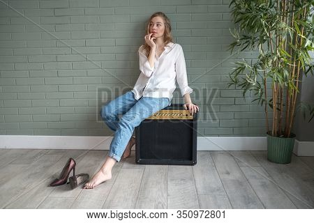 Young Beautiful Woman Sitting On Subwoofer With Bare Feet Next To Green Plant