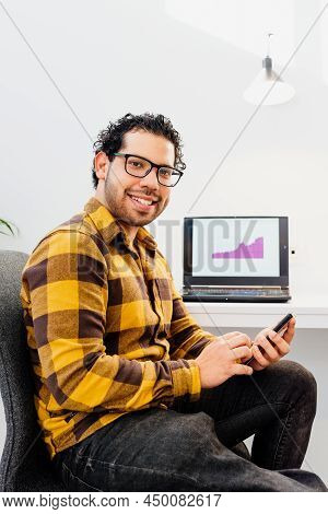 Portrait Of Brazilian Man With Glasses And Leg Handicap At Workplace Using Smartphone And Checking S