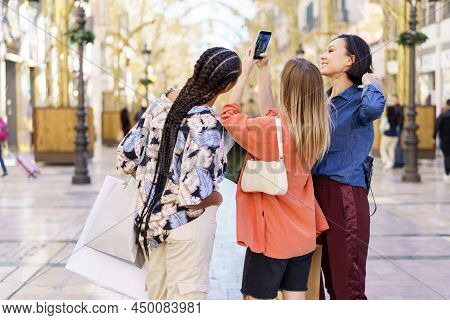 Back View Of Young Multiracial Female Friends Wearing Trendy Outfits Standing With Shopping Bags And
