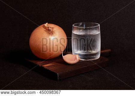 Still Life On A Dark Background. A Glass Of Vodka, Onion And Garlic On A Wooden Stand