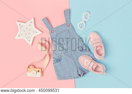 Stylish Summer Set Of Child Clothes. Denim Jumpsuit, Pink Sneakers And Accessories On A Pink Blue Ba