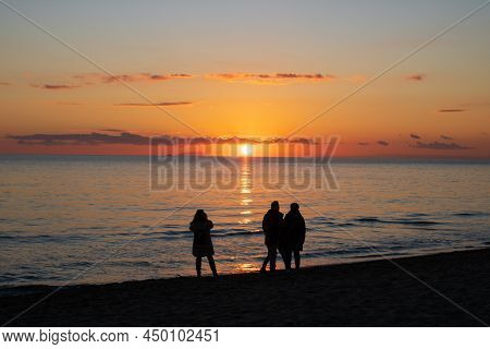 Three Peolple Walking On A Beach Under Sunset