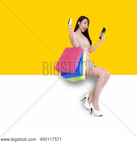 Happy Young Woman Sitting On Blank Banner. Shopping Online With Mobile Phone Concepts
