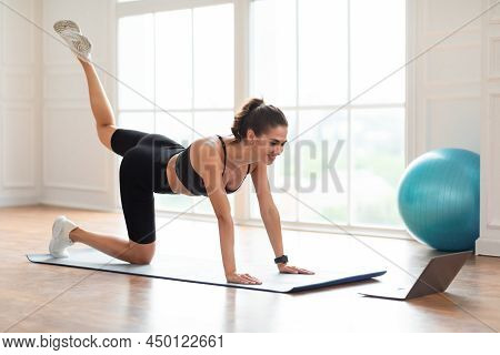 Smiling Woman In Sportswear Doing Donkey Kicks Exercise Using Pc