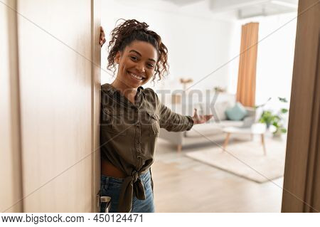 Joyful Millennial Black Lady Opening Door Welcoming Standing At Home