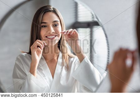 Oral Care. Smiling Young Female Using Dental Floss Near Mirror In Bathroom