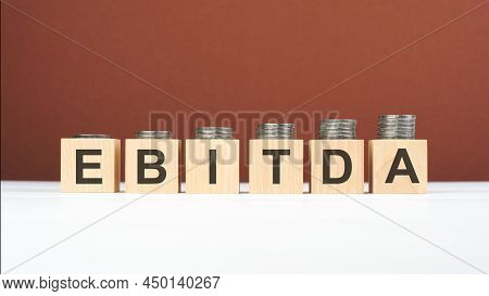 Ebitda Text On Wooden Blocks With Coins On Brown Background, Business Concept. Ebitda - Short For Ea