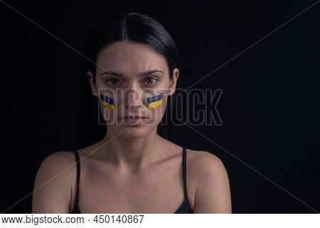 Portrait Of Serious Ukrainian Woman With Blue And Yellow Ukrainian Flag On Her Cheek. The Symbol Of 