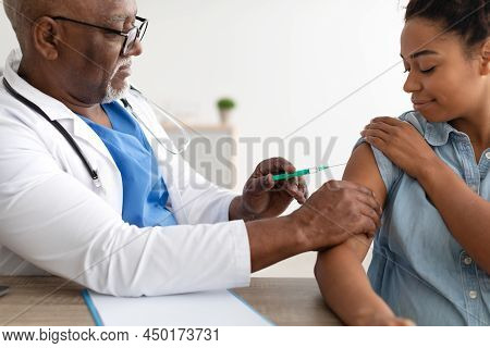 Black Woman Receiving Vaccine Injection Sitting With Doctor Indoor