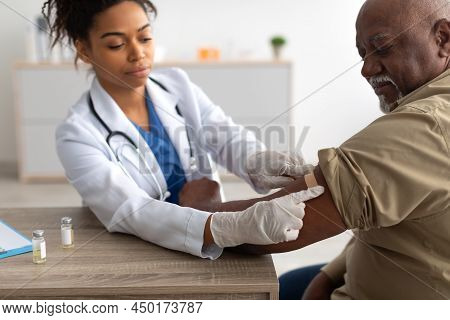 Black Mature Man Getting Vaccinated, Doctor Applying Adhesive Bandage