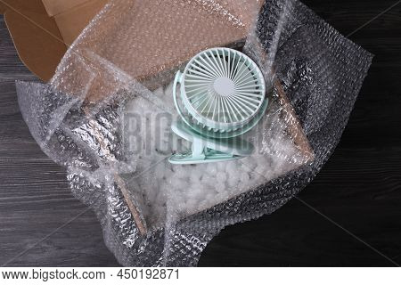 Small Fan With Bubble Wrap And Packaging Foam In Cardboard Box On Dark Wooden Table, Top View