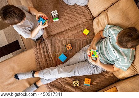 Top View Two Teenage And Baby Brothers Assembling Multicolored Rubiks Cubes Sitting On Couch