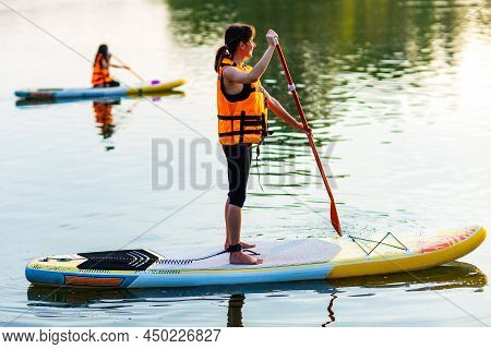 Young Woman In Orange Life Jacket On Supboard At River