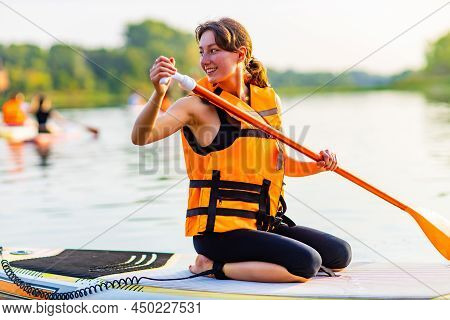 Young Woman In Orange Life Jacket On Supboard At River