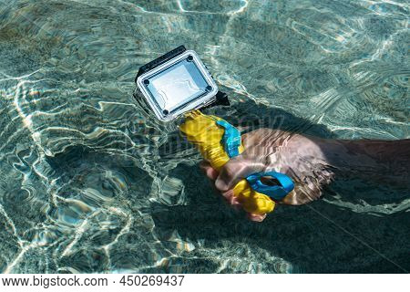 Action Camera In The Hands Of A Man On A Warm Sunny Day. Against The Backdrop Of Clear Water.