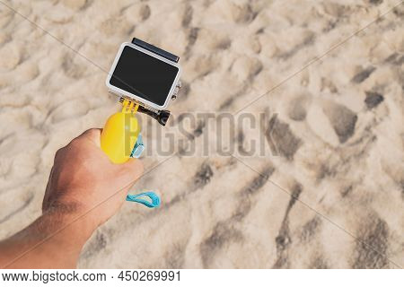Action Camera In The Guy's Hand. Against The Backdrop Of A Sandy Beach Close-up.