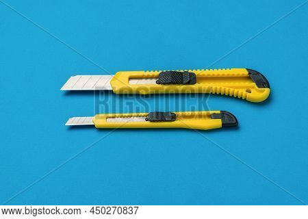 Two Yellow Paper Knives With Extended Blades On A Blue Background. Minimalistic Concept.