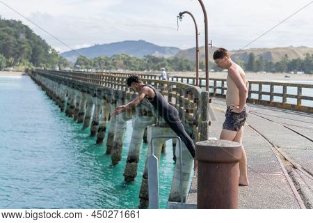 Tolaga Bay. New Zealand - February 5 2022; One Boy Watches As Another Dives Off The Wharf High Above