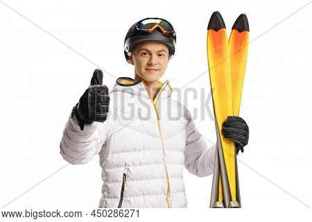 Guy with ski goggles and jacket holding a pair of skiis and gesturing thumbs up isolated on white background