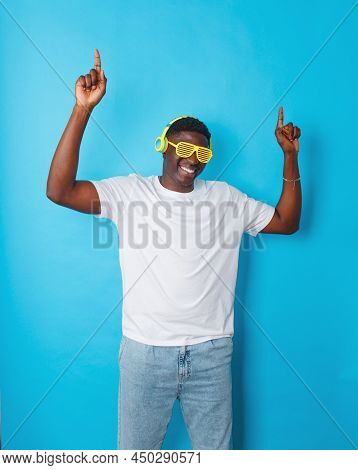 An African-american Man Is Dancing Merrily In Yellow Headphones And Stylish Glasses On An Isolated B