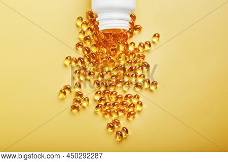 Gold Vitamin D3 Capsules Poured Out Of A Jar On A Yellow Background With Free Space