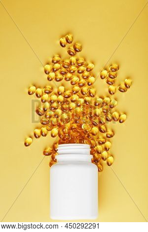 Golden Omega-3 Fish Oil Capsules Poured Out Of A Jar On A Yellow Background