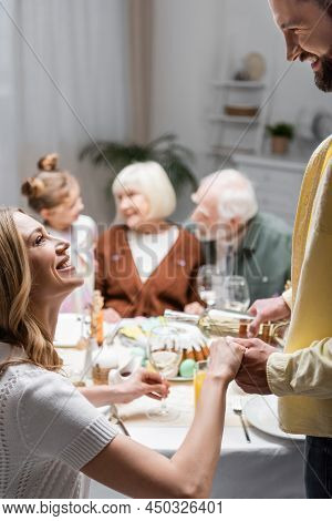 Smiling Woman Holding Hand Of Husband Pouring Wine During Easter Dinner.