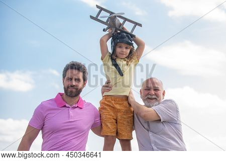 Three Different Generations Ages Grandfather Father And Child Son Playing With Toy Plane Outdoors. S