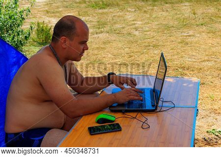 Man Using His Laptop Sitting At A Folding Picnic Table In A Camping. Working While Traveling. Freela