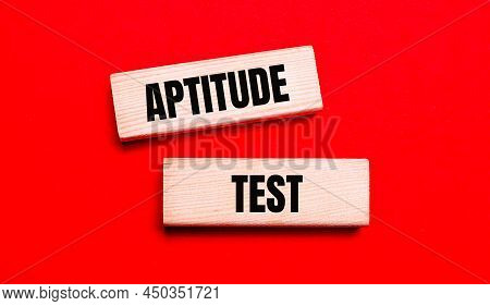 On A Bright Red Background, There Are Two Light Wooden Blocks With The Text Aptitude Test