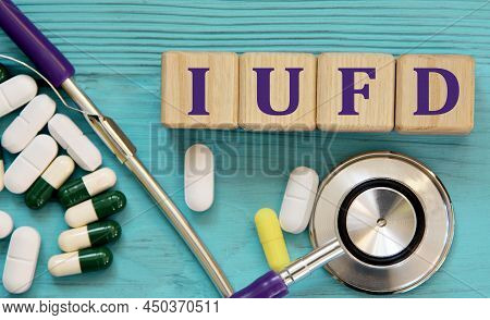 Iufd (intrauterine Fetal Demise) - Acronym On Wooden Cubes On A Blue Background With A Stethoscope A