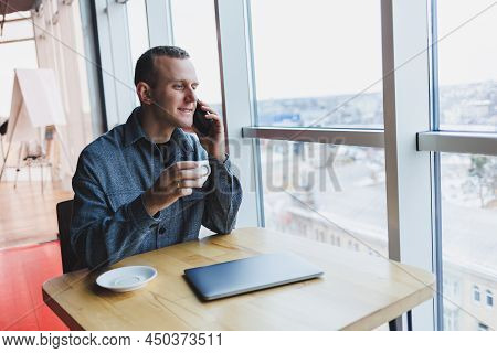Happy Man With Coffee Calling Via Smartphone While Remote Working Laptop At Work Desk, Cheerful Free
