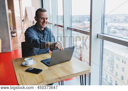 Successful Happy Business Man Is Sitting At A Table In A Cafe, Holding A Cup Of Coffee And Using A L