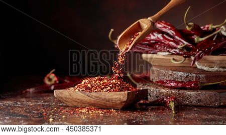 Chilli Flakes Are Poured Into A Wooden Dish. Chilli Flakes And Dried Chili Peppers On A Brown Backgr