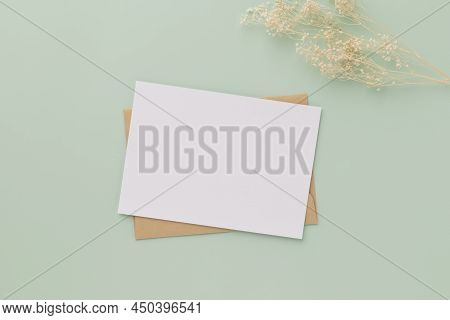 Blank Greeting Card Invitation Mockup 5x7 On Brown Envelope With Dried Flowers On Pastel Green Backg
