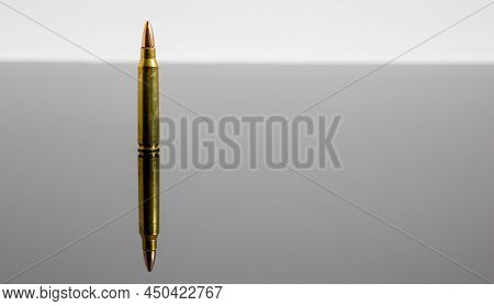 Single 5.56 Round On Dark Reflective Surface And White Background