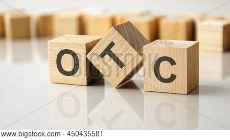 Three Wooden Cubes With The Letters Otc On The Bright Surface Of A Gray Table. The Inscription On Th
