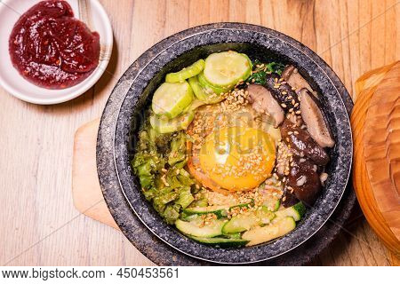 Bibimbap In A Black Heated Stone Bowl, Korean Traditional Dish- Bibimbap Mixed Rice With Vegetables 