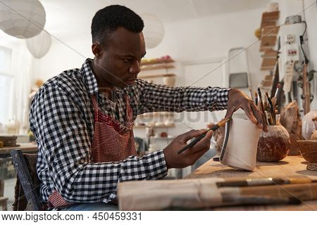 Focused Ceramist Painting Unglazed Piece Of Pottery