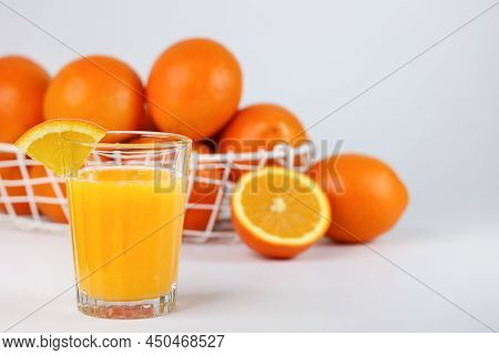 A Glass Of Fresh Orange Juice And A Basket With Fresh Oranges