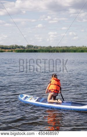 Little Girl On Sup Board Kneeling Looking At Water Surface With Puddle In Right Hand Put In Water We