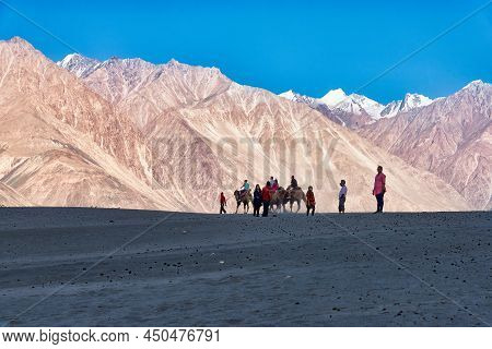 Hunder, India - August 19, 2015: Group Of People Riding Bactrian Camels In Sand Dunes In Nubra Valle