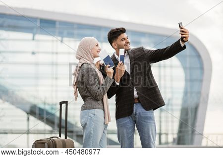 Joyful Muslim Couple Ready For Trip, Taking Selfie Outdoors Near Airport Terminal, Happy Smile And G