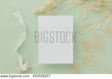 Blank Greeting Card Invitation Mockup 5x7 On Brown Envelope With Dried Flowers On Pastel Green Backg
