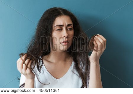Dryness And Dandruff. A Young Caucasian Woman Looks Thoughtfully At The Tips Of Her Disheveled Long 