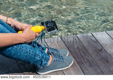 Action Camera In The Hands Of A Girl. Against The Backdrop Of A Wooden Deck, A Tabletop On The Surfa