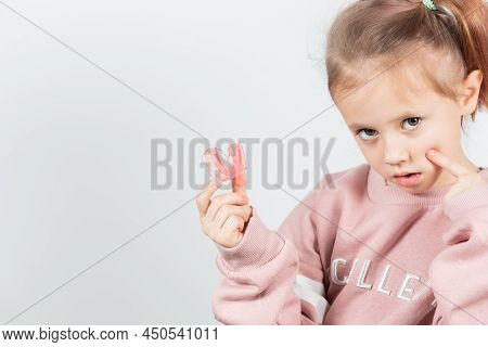 Cute Little Girl With Blond Hair Is Holding A Pink Dental Myofunctional Trainer
