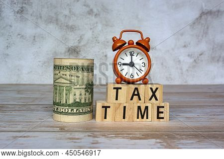 Tax Time Text On Wooden Blocks And Alarm Clock Set At 9 O'clock With Banknotes On Table. Business An