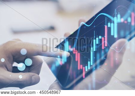 Close Up Of Hand Using Digial Tablet At Desktop With Glowing Forex Chart On Blurry Background. Trade